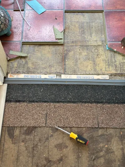 Close-up of a roof edge mid-shingle-replacement above a tiled patio, with a screwdriver resting on the new shingles.