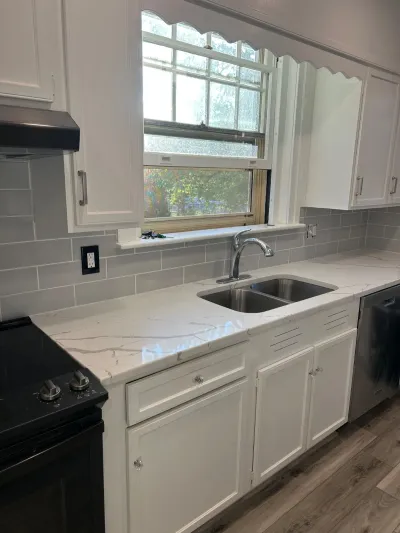 Renovated kitchen counter with white cabinets, marble-look countertop, and subway tile backsplash near a window.