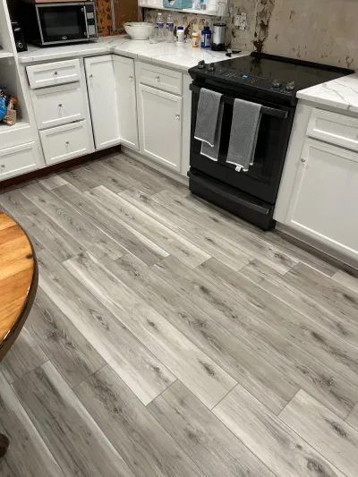 Kitchen mid-renovation with new wood-look flooring, white cabinets, and an unfinished wall above the counter.