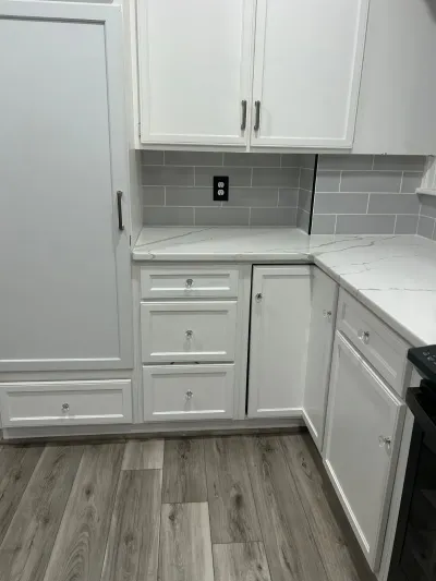Corner of a white kitchen with grey subway tile backsplash, quartz counters, and wood-look plank flooring.