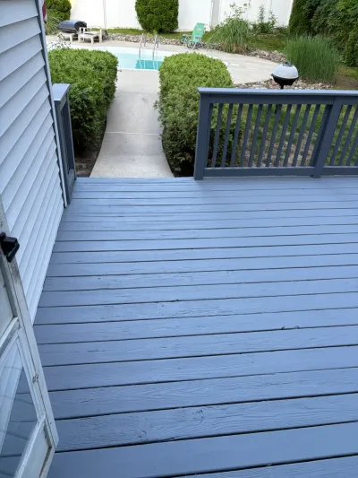Painted grey wood deck with railing overlooking a landscaped path to an in-ground pool.