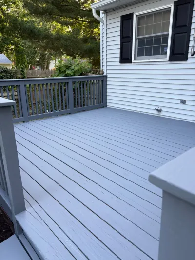A newly painted grey wood deck attached to a house with white siding and black window shutters.