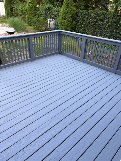 A freshly painted gray wood deck with matching railing overlooking a backyard with greenery.