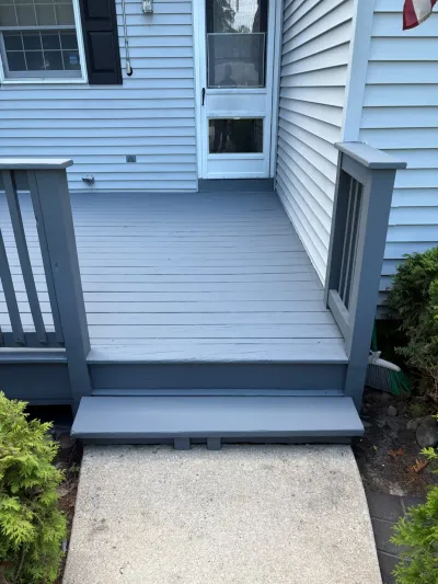 Grey-painted wood deck and steps leading to a white house's side entry door.