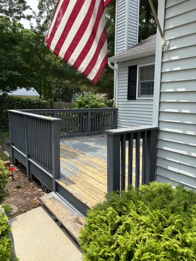 A weathered wood deck with peeling paint attached to a house with vinyl siding and an American flag.