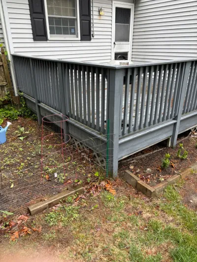 Weathered grey wood deck attached to a house, with an unfinished garden bed and wire fencing in front.