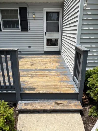 Weathered deck with peeling grey paint exposing bare wood, next to a home's side entry door.