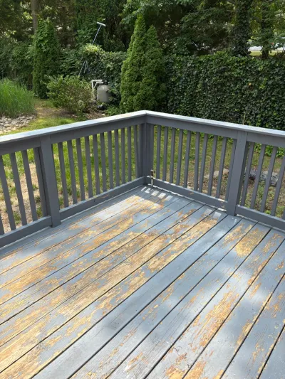 Weathered deck with peeling grey paint on the floorboards, overlooking a backyard with hedges.