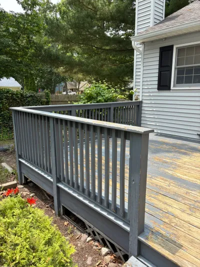 A weathered wood deck with peeling gray paint attached to a house with vinyl siding, before renovation.