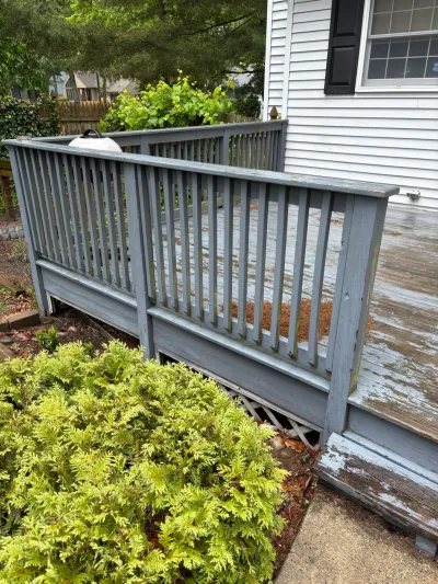 Weathered deck with peeling grey paint, worn boards, and damaged lattice skirting beside a house.