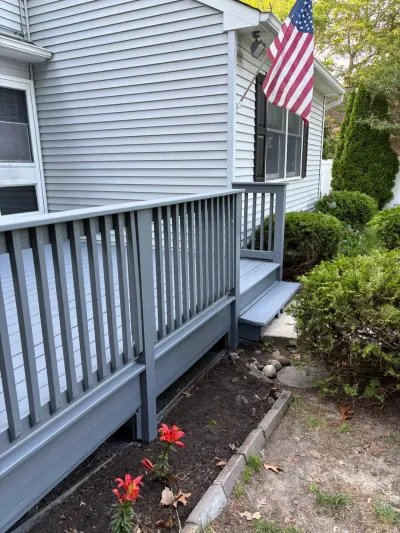 Side view of a house with gray siding, a painted blue-gray deck, and a garden bed with orange daylilies.