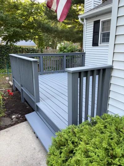 A newly painted slate-grey wood deck with railings attached to a white house, leading down painted steps to a walkway.