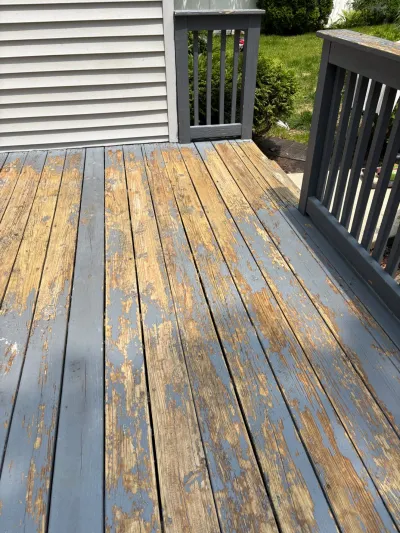 A wood deck with heavily peeling grey paint exposing bare wood, next to a painted railing.