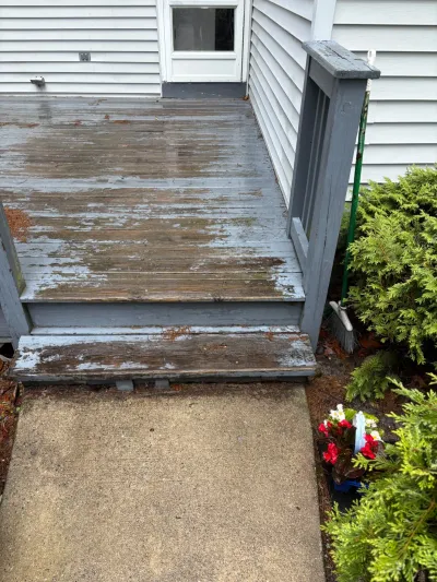Weathered wood deck and steps with heavily peeling grey paint leading to a concrete walkway.