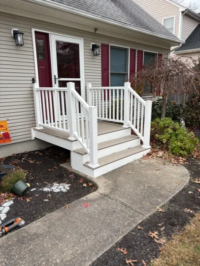 New composite deck stairs with white vinyl railing leading to a home's front entry.