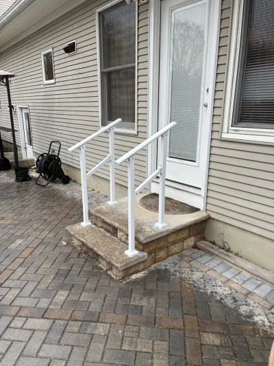 Back entry steps with white handrails, stone veneer risers, and a paver patio outside a vinyl-sided home.