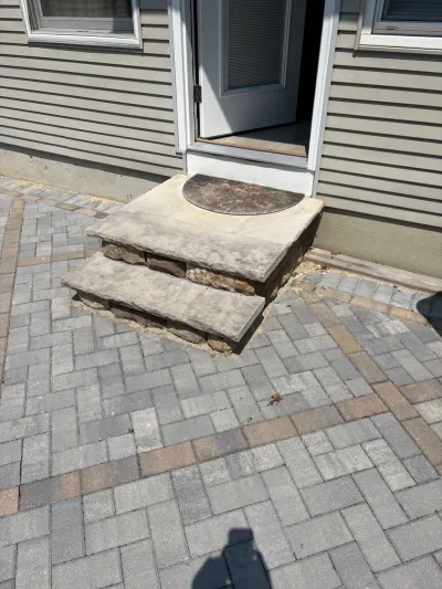 Finished paver patio with a two-step stone entry stoop leading to an open exterior door.