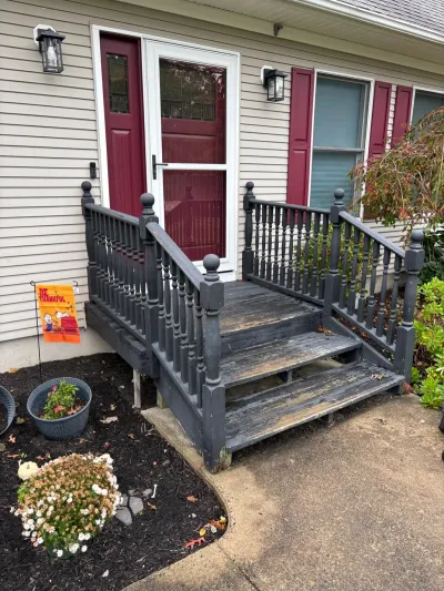 Weathered wooden porch steps with peeling gray paint lead to a red front door with fall decorations nearby.