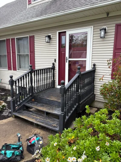Weathered front porch with peeling black railings and worn wooden steps before renovation.