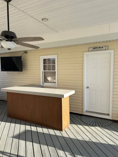 Covered outdoor deck with a built-in bar, ceiling fan, wall-mounted TV, and a white entry door.