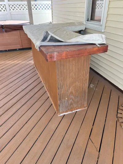 Weathered wood deck with a built-in hot tub, its cover partially folded back, beside the house siding.